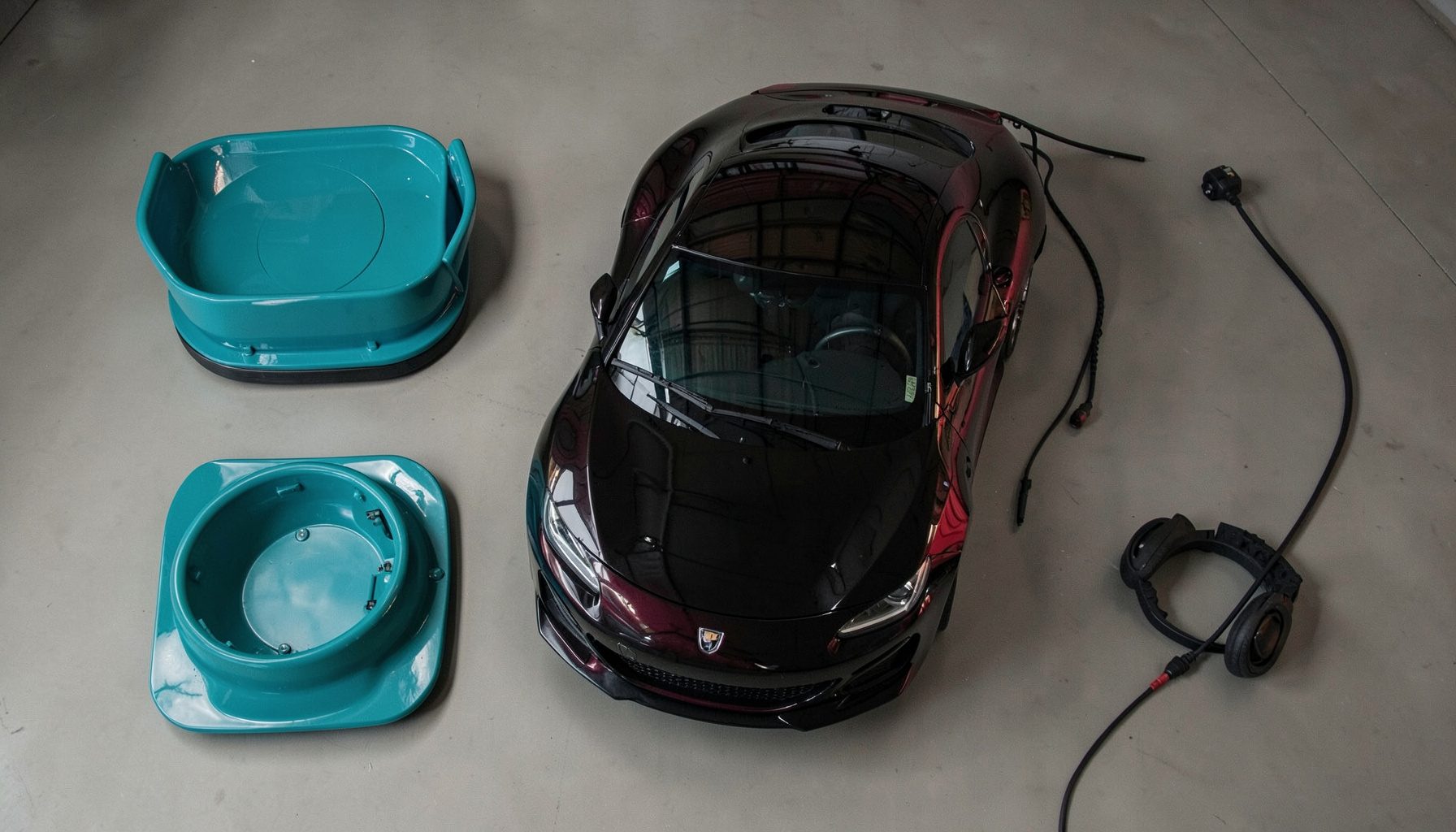 Berline sportive sous éclairage tamisé dans un hangar, carrosserie sombre, reflets rouges et noirs.